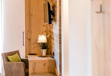 A modern furnished room with wooden accents. There is a lamp on a desk and a television is mounted.