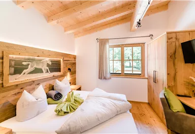 A cozy bedroom with wooden paneling and a large window. The room is bright and inviting, furnished with comfortable pillows and blankets.