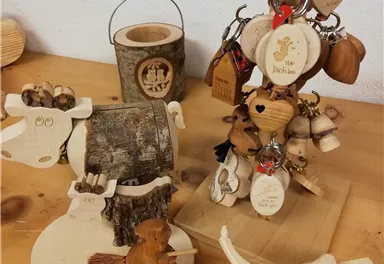 Eine Sammlung von handgefertigten Holzschmuckstücken und Schlüsselanhängern. Dazu gehören Tiere und kleine Holzfiguren, die auf einem Tisch ausgestellt sind.