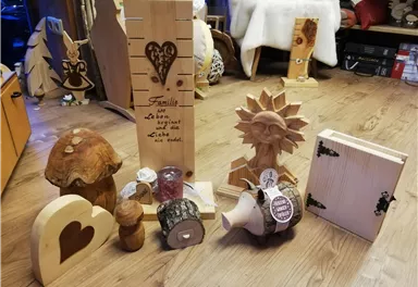 Eine Ansammlung von handgefertigten Holzdekoartikeln. Darunter befinden sich eine herzförmige Figur, eine Sonne, und verschiedene andere Skulpturen und Behälter.