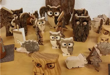 Eine Sammlung von handgefertigten Holzfiguren in Form von Eulen und anderen Tieren. Die Figuren sind unterschiedlich groß und aus verschiedenen Holzarten gefertigt.