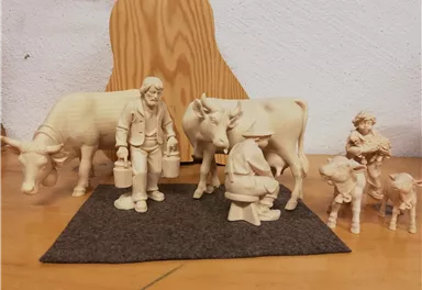 Eine Gruppe von geschnitzten Figuren zeigt Bauern mit Kühen und kleinen Tieren. Die Szene ist handwerklich gestaltet und vermittelt ländliches Leben.