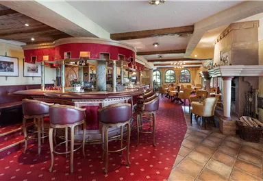 A cozy dining area with a wooden bar and round tables. The decor is in warm colors, creating an inviting atmosphere.