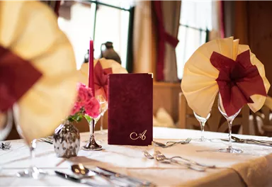 An elegantly set table with a menu card and decorative napkins. Flowers and candles create a festive atmosphere.