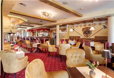 A cozy restaurant with comfortable yellow armchairs and a warm ambiance. The room is stylishly decorated and has an inviting bar.