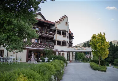 A charming hotel with traditional architecture and colorful flowers in the garden. Surrounded by trees, it offers a tranquil atmosphere.