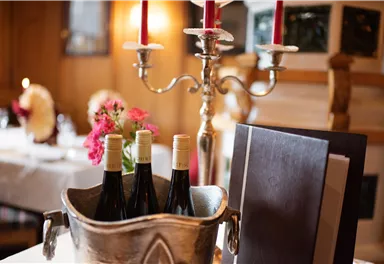 An elegant table with a silver wine cooler containing three bottles of wine. In the background, there are candles and fresh flowers.