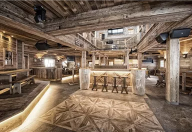 A stylish restaurant with rustic wooden interiors and a cozy atmosphere. The bar is centrally located and surrounded by comfortable seating areas.