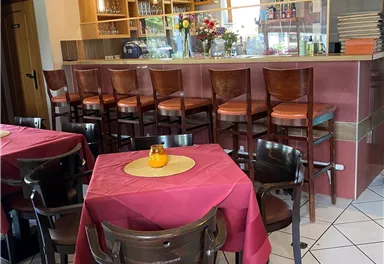 Ein gemütliches Restaurant mit rot eingedeckten Tischen und einer Holzbar. Die Atmosphäre ist einladend und freundlich.