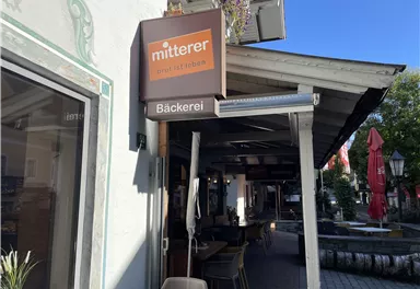 A cozy café with a bakery on the facade. Tables and chairs are outside under a canopy.
