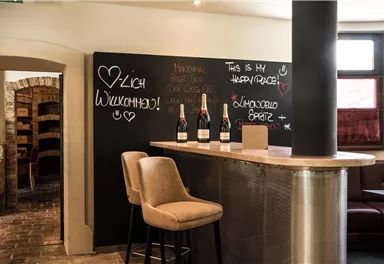 Eine stilvolle Bar mit einer Willkommensnachricht auf einer Tafel. Auf dem Tresen stehen Flaschen, umgeben von modernem Interieur.