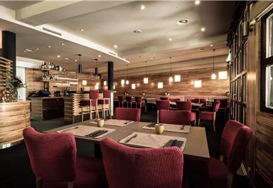 Ein modernes Restaurant mit Holzdetail und bequemen roten Stühlen. Die Beleuchtung ist angenehm und schafft eine einladende Atmosphäre.
