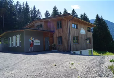 A modern wooden house in a mountainous area. The entrance is friendly and surrounded by trees.