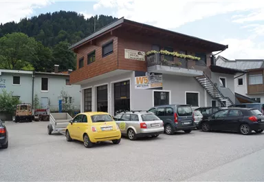 A modern building with wooden cladding in a rural setting. Several cars are parked in the parking lot, including a yellow car.