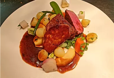 Ein kunstvoll angerichtetes Gericht mit zartem Fleisch, buntem Gemüse und einer reichhaltigen Sauce. Die Kombination aus verschiedenen Texturen und Farben sorgt für einen ansprechenden Look.