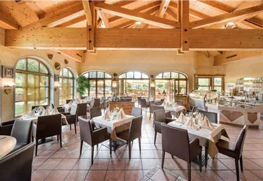 A cozy restaurant with a wooden ceiling and large windows. The tables are elegantly set and offer a view of the outside.