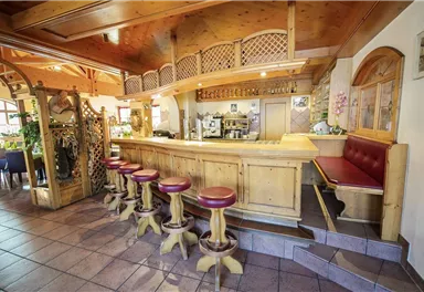A cozy bar with wooden paneling and red bar stools. In the background, a coffee machine and seating are visible.