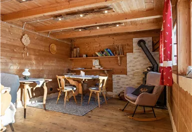 Ein gemütlicher Holzraum mit einem Esstisch und Stühlen. An der Wand befindet sich ein Kamin, und die Fenster sind mit roten Vorhängen geschmückt.