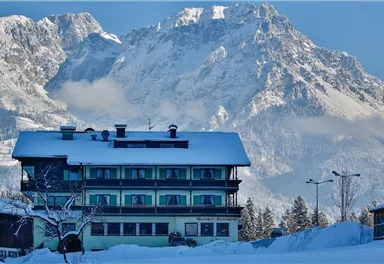 A charming hotel in winter with a snow-covered roof. In the background, majestic mountains rise.