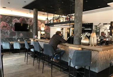 A stylish café with a modern bar and elegant chairs. Decorative floral patterns can be seen on the wall in the background.