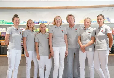 A team of seven people stands in front of a shelf of health products. They are all wearing gray polo shirts and white pants.
