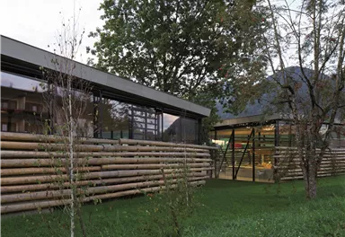 A modern building with a glass facade and wooden cladding. Surrounded by trees and green grass.