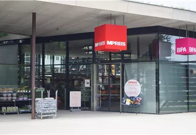 A modern supermarket with large glass windows and an inviting entrance. Above the entrance hang red signs of the brands MPREIS and BIPA.