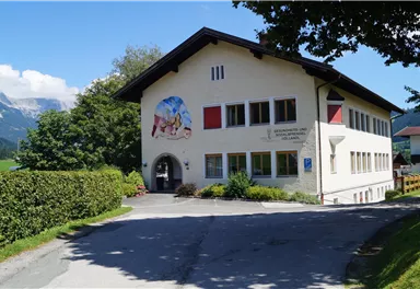 A beautiful building in a rural setting with a painting on the wall. There are trees and a quiet road leading to the building.