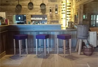 A cozy wooden bar with four stools and a warm atmosphere. In the background, there are shelves with drinks and an inviting counter.