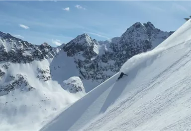 Eine wunderschöne winterliche Berglandschaft mit schneebedeckten Gipfeln. Ein Skifahrer fährt die Piste hinunter und hinterlässt eine Spur im frischen Schnee.