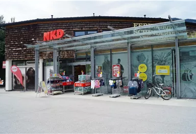 A store of NKD with a modern glass façade. In front of the shop are clothes and advertising boards with offers.