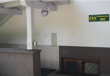 Ein Zugang zu öffentlichen Waschräumen ist sichtbar. Neben dem Eingang hängt ein Schild mit Weghinweisen.