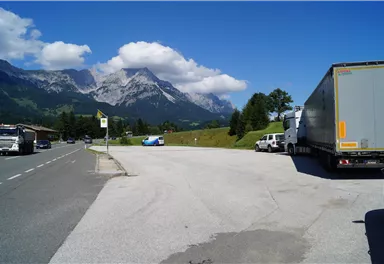 A clear view of majestic mountains under a blue sky. Some vehicles are parked by the roadside in a tranquil setting.