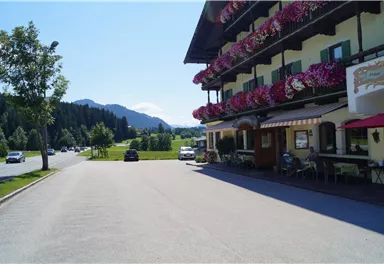 A picturesque inn with colorful flower balconies. In the background, green meadows and mountains are visible.