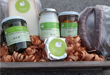 A basket with various foods, including cheese, yogurt, and pickled vegetables. Everything is nicely arranged in a bed of paper strips.