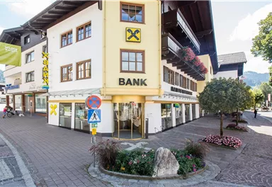 Ein modernes Bankgebäude an einer Straßenecke. Blumenrabatte und eine klare Himmelssicht runden die Szene ab.