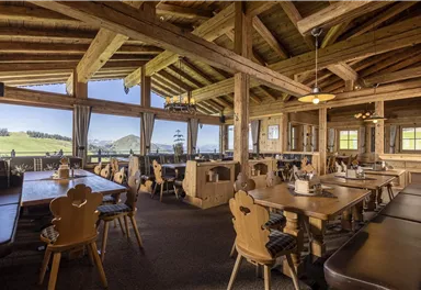 A cozy restaurant with wooden furniture and large windows. The view of the green landscape creates an inviting atmosphere.