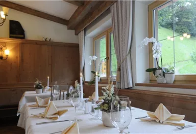 Ein gemütliches Esszimmer mit einem schön gedeckten Tisch. Die Fenster lassen viel Licht herein und bieten Blick auf die grüne Landschaft.