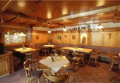 A cozy restaurant with wooden interiors and tables. The walls are adorned with artworks and decorative elements.