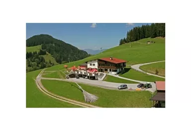 A picturesque mountain cabin with a red roof amidst green meadows. The surroundings are hilly and wooded, ideal for a relaxing stay in nature.