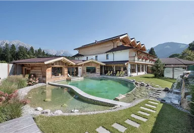 Ein modernes Haus mit Holzdetails und einem großen Garten. Der Garten verfügt über einen Schwimmteich und ist von Bergen umgeben.