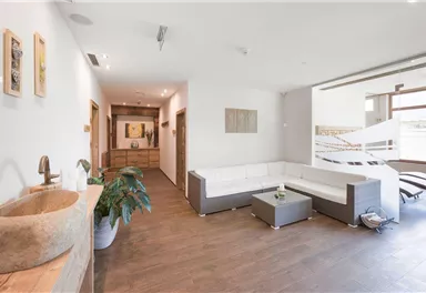 Ein moderner Wohnraum mit einem eleganten Sofa und Holzfußboden. Es gibt Pflanzen und Kunstwerke an den Wänden, die eine einladende Atmosphäre schaffen.