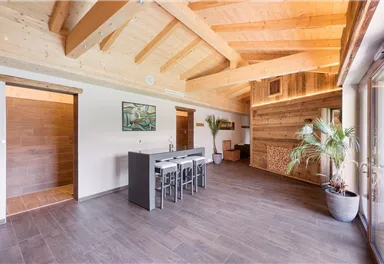 Ein modernes, helles Zimmer mit Holzdecke und großen Fenstern. Es gibt einen Esstisch mit Stühlen und eine kleine Pflanze in der Ecke.