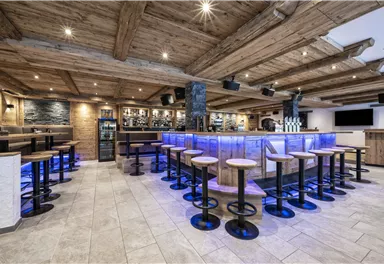 A modern bar with wooden decor and atmospheric lighting. The seating is arranged around the central bar.
