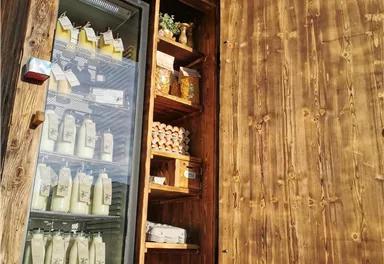 A wooden stand with an open door, offering dairy products and fresh groceries. The refrigerator is visible and displays many bottles in the showcase.