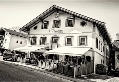 A traditional Bavarian inn with a distinctive architectural style. The facade is in black and white, and there is a terrace with outdoor seating.