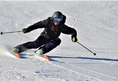 Ein Skifahrer fährt auf einer verschneiten Piste. Er ist in voller Ausrüstung und macht eine schnelle Kurve.