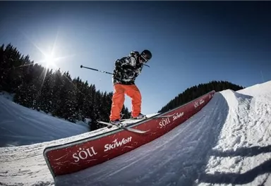 A skier is riding on a snowboard ramp in the snow. The clear sky and the trees in the background create a lovely winter atmosphere.