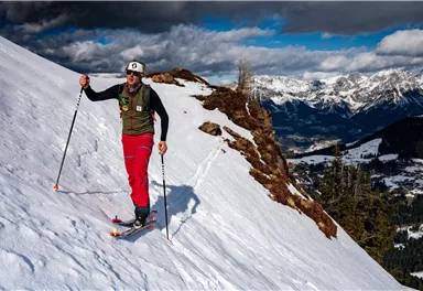 A skier is riding down a snow-covered slope. In the background, impressive mountains and a clear sky can be seen.