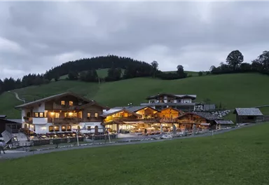 A picturesque alpine building at dusk, surrounded by gentle hills. The lights in the building create an inviting atmosphere.